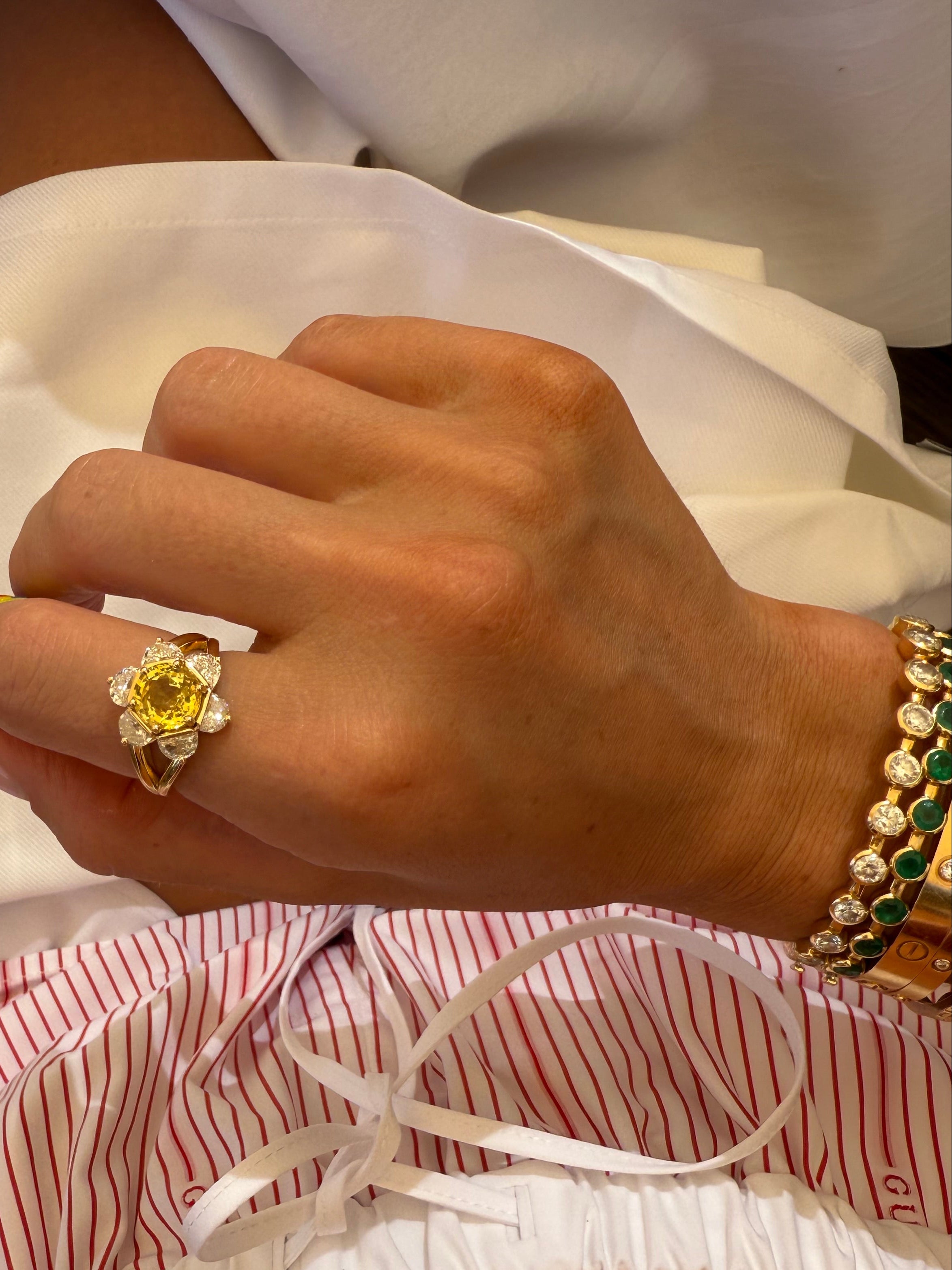 Close-up of a hand wearing a yellow sunflower gemstone ring with a white and red striped garment in the background.
